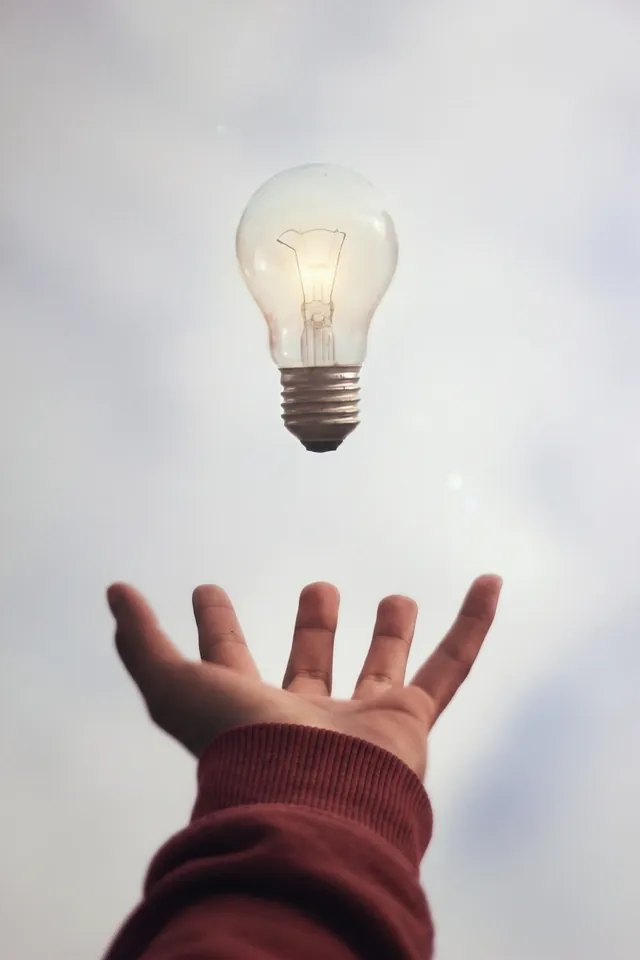 Main tendue vers une ampoule suspendue dans le ciel